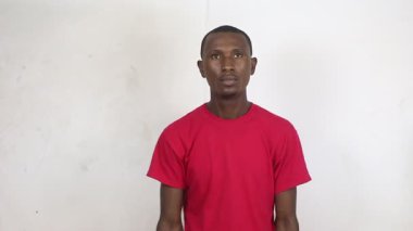 Beyaz arka planda duran kırmızı tişörtlü genç adam parmağıyla bir şey gösterecek ve zafer jesti yapıp gülecek..