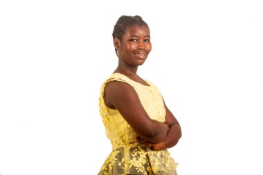 Sarı elbiseli genç bir kız beyaz bir arka planda durup kollarını kavuşturmuş gülümseyen kameraya bakıyordu..