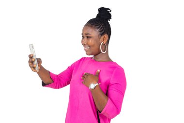 Pembe gecelikli genç bir kız beyaz arka planda duruyor cep telefonuna bakıyor ve gülüyor..