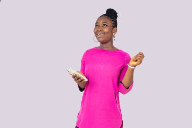 Beyaz arka planda duran pembe gecelikli genç bir kız elinde cep telefonuyla gülüyor..