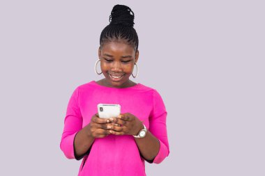 Pembe paçalı güzel bir öğrenci beyaz arka planda durup gülümserken cep telefonunu tutuyor..