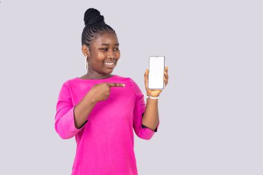 Pembe paçalı güzel bir kız öğrenci beyaz arka planda durup gülerken cep telefonunu gösteriyor..