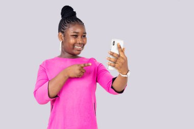 Pembe gecelikli güzel bir kız beyaz arka planda duruyor cep telefonuna gülümsüyor..