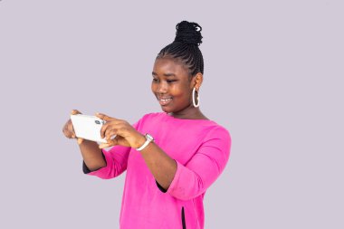 Beyaz arka planda duran pembe gecelikli güzel bir kız elinde cep telefonuyla gülümsüyor..