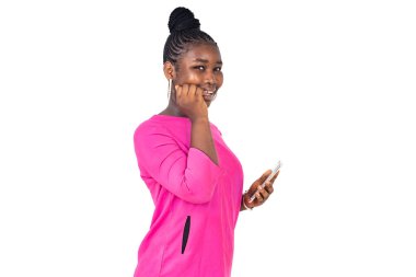 Pembe paçalı güzel bir genç kız beyaz bir arka planda, parmakları ağzında bir cep telefonu tutuyor ve gülümsüyor..