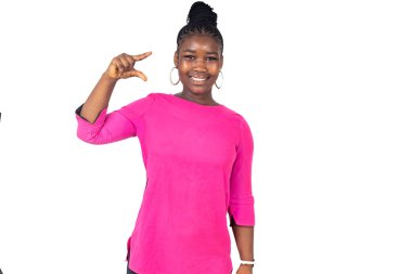 Pembe paçalı genç bir kız öğrenci beyaz arka planda duruyor. İki parmağıyla küçük belini gösterirken gülümsüyor..