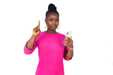 Pembe paçalı genç bir kız beyaz arka planda duruyor. Cep telefonu işaret ediyor..