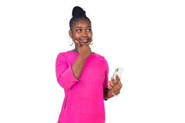 Beyaz arka planda duran pembe gecelikli genç bir kız düşünceli bir bakışla cep telefonunu tutuyor..