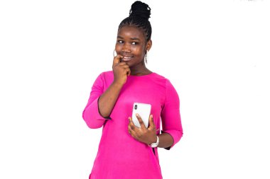 Beyaz arka planda duran pembe gecelikli genç bir kız düşünceli bir bakışla cep telefonunu tutuyor..