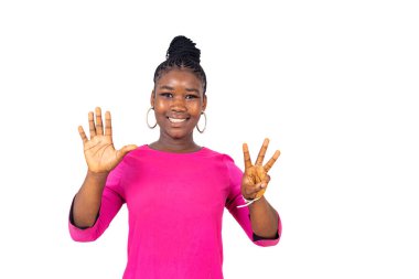 Beyaz arka planda duran pembe gecelikli genç bir kız parmaklarını sayıyor ve gülümseyen kameraya bakıyor..