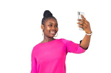 Beyaz arka planda duran pembe gecelikli genç bir kız gülümserken cep telefonuyla video görüşmesi yapıyor..