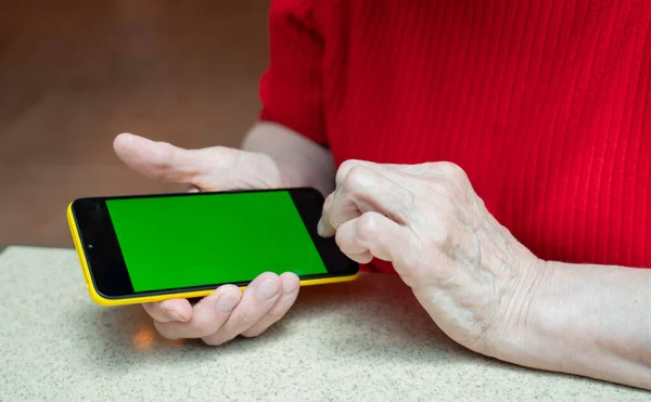 Phone with a green screen in the arm of an elderly woman of retirement age. High quality photo