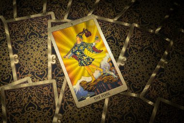 Masada altın işlemeli tarot kartları var. Binbaşı Arcana kartı. Aptal, izleyiciye bakıyor. Yüksek kalite fotoğraf
