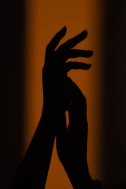 Siluet, batan güneşin turuncu ışınlarında duvarda bir kadının elinin gölgesi. Görüntü olarak soyut arkaplan, odak dışı. Yüksek kalite fotoğraf