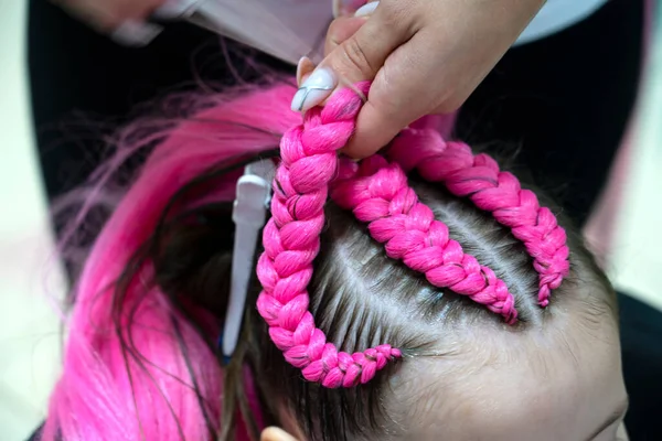 Bir kız için parlak pembe ve mavi kanekalondan moda örgüler örme süreci. Okula dönelim. Braid stüdyosu. Yüksek kalite fotoğraf