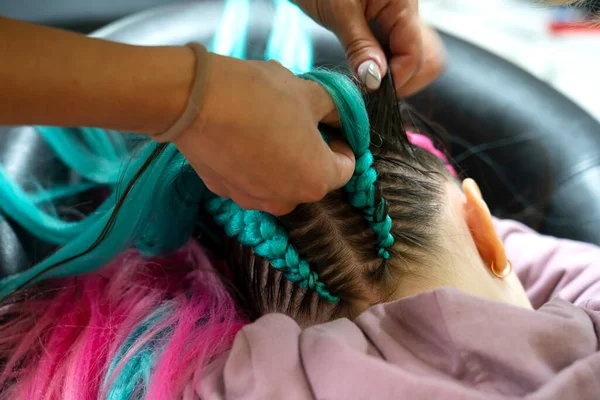 Pembe ve mavi kanekalon örgülü bir kız için şık bir saç stili. Kuaför kafasının arkasına örgü örer. Okula dönelim. Braid stüdyosu. Yüksek kalite fotoğraf