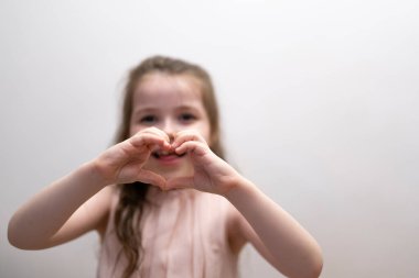 Bir kız, yedi yaşında bir esmer, elleriyle bir kalp figürü gösteriyor. Yüksek kalite fotoğraf
