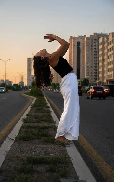 stock image Young Asian woman practicing yoga outdoor during daytime with the view of the city. The girl practices yoga on the street. Urban yoga, sunrise workout.