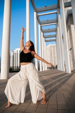 Genç Asyalı kadın gündüz vakti şehir manzarasıyla yoga yapıyor. Kız mavi gökyüzü manzaralı asanas gösterisi yapıyor. Şehir yogası, gün doğumu egzersizi. Şehir yogası, gün doğumu egzersizi..