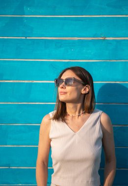 Güneş gözlüklü esmer bir kadının yaz portresi mavi ahşap arka planda yazı için yeri olan bir kadına karşı. Yüksek kalite fotoğraf