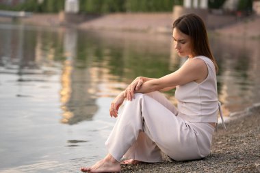 Yazın esmer bir kadının şehir portresi. Kadın nehrin kıyısında oturur ve bir şey düşünür. Yüksek kalite fotoğraf