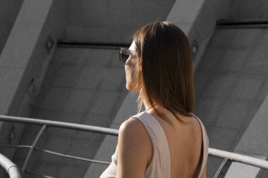 Genç esmer kadının şehir yaz portresi. Arkasında beton bir duvar olan bir kadın köprüde duruyor. Yüksek kalite fotoğraf