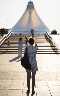 Astana 'daki Khan-Shatyr alışveriş merkezinin karşısındaki meydanda genç bir kadın duruyor. Yüksek kalite fotoğraf