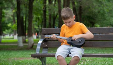 Elinde ukulele olan sekiz yaşında sarışın bir çocuğun sokak portresi. Konsept: müzik enstrümanları çalmayı öğrenmek, müzik aşığı, gitar çalmak, kullanışlı eğlence. Yüksek kalite fotoğraf