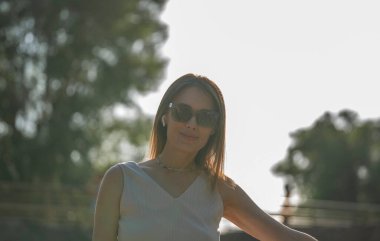 Güneş gözlüklü esmer bir kadının yaz şehir portresi. Portre, altın saat boyunca arka planda çekildi. Yüksek kalite fotoğraf