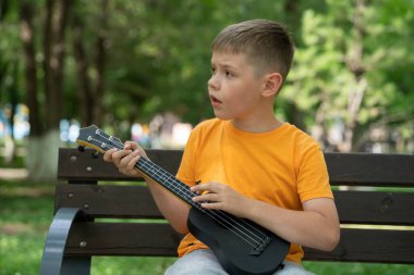 Elinde ukulele olan sekiz yaşında sarışın bir çocuğun sokak portresi. Konsept: müzik enstrümanları çalmayı öğrenmek, müzik aşığı, gitar çalmak, kullanışlı eğlence. Yüksek kalite fotoğraf