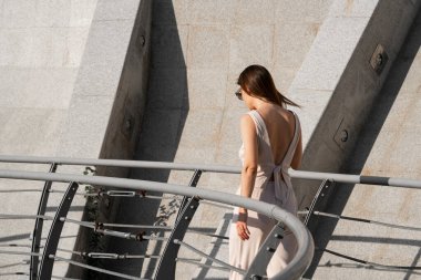 Genç esmer kadının şehir yaz portresi. Arkasında beton bir duvar olan bir kadın köprüde duruyor. Yüksek kalite fotoğraf