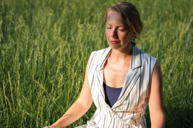 Genç sarışın bir kadın öğle yemeği molası sırasında parkta çimenler üzerinde meditasyon yapıyor. Yüksek kalite fotoğraf