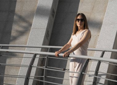 Genç esmer kadının şehir yaz portresi. Arkasında beton bir duvar olan bir kadın köprüde duruyor. Yüksek kalite fotoğraf