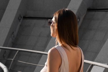 Genç esmer kadının şehir yaz portresi. Arkasında beton bir duvar olan bir kadın köprüde duruyor. Yüksek kalite fotoğraf