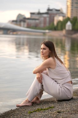 Yazın esmer bir kadının şehir portresi. Kadın nehrin kıyısında oturur ve bir şey düşünür. Yüksek kalite fotoğraf