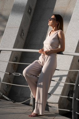 Genç esmer kadının şehir yaz portresi. Arkasında beton bir duvar olan bir kadın köprüde duruyor. Yüksek kalite fotoğraf