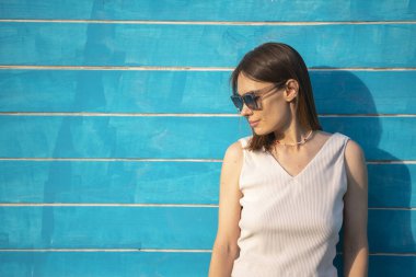 Güneş gözlüklü esmer bir kadının yaz portresi mavi ahşap arka planda yazı için yeri olan bir kadına karşı. Yüksek kalite fotoğraf