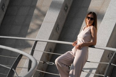 Genç esmer kadının şehir yaz portresi. Arkasında beton bir duvar olan bir kadın köprüde duruyor. Yüksek kalite fotoğraf