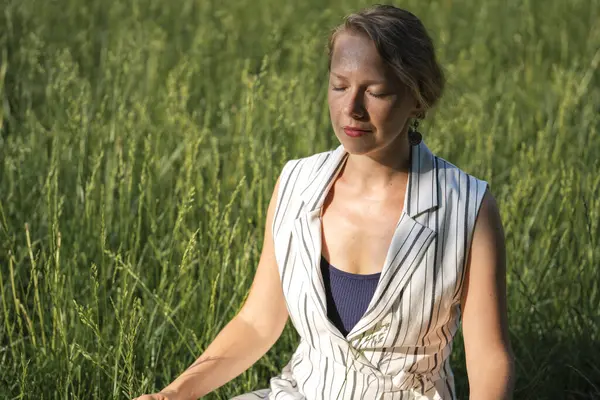 Genç sarışın bir kadın öğle yemeği molası sırasında parkta çimenler üzerinde meditasyon yapıyor. Yüksek kalite fotoğraf