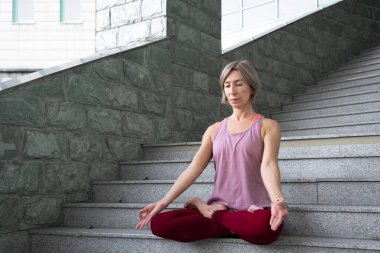 59 yaşında, merdivenlerde lotus pozisyonunda oturup meditasyon yapan olgun bir kadının portresi. Olgun insanların aktif spor yaşam tarzı. Yüksek kalite fotoğraf