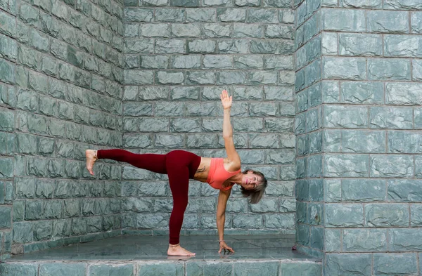 Portrait of a mature woman 59 years old doing yoga asanas against the gray wall of the building. Active sport lifestyle of mature people. High quality photo