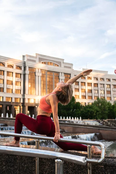 Portrait of a mature woman, 59 years old, doing yoga near the city fountain. Active sport lifestyle of mature people. Sports in the life of a senior woman.