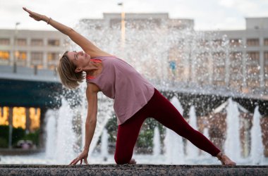 59 yaşında, şehir çeşmesinin yanında yoga yapan olgun bir kadının portresi. Olgun insanların aktif spor yaşam tarzı. Son sınıf bir kadının hayatında spor.. 
