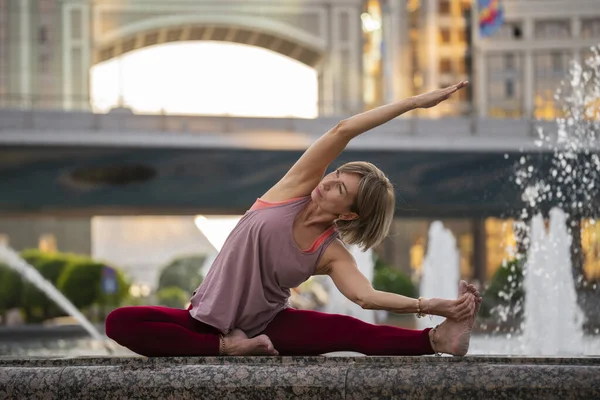 Portrait of a mature woman, 59 years old, doing yoga near the city fountain. Active sport lifestyle of mature people. Sports in the life of a senior woman.