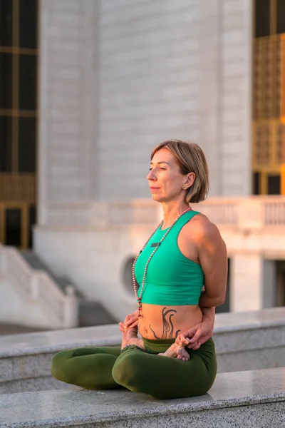 Portrait of a mature woman, 59 years old, doing yoga on a city street. Active sport lifestyle of mature people. Sports in the life of a senior woman.