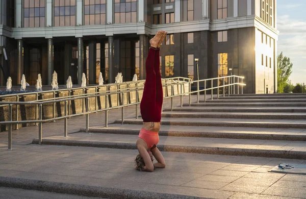 Portrait of a mature woman, 59 years old, doing yoga on a city street. Active sport lifestyle of mature people. Sports in the life of a senior woman. Woman doing a headstand.