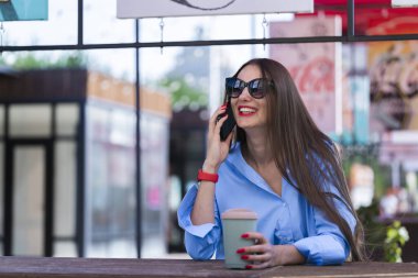Uzun sarı saçlı bir kızın yaz portresi. Mavi gömlekli ve güneş gözlüklü bir kız akıllı telefondan konuşuyor. Yüksek kalite fotoğraf