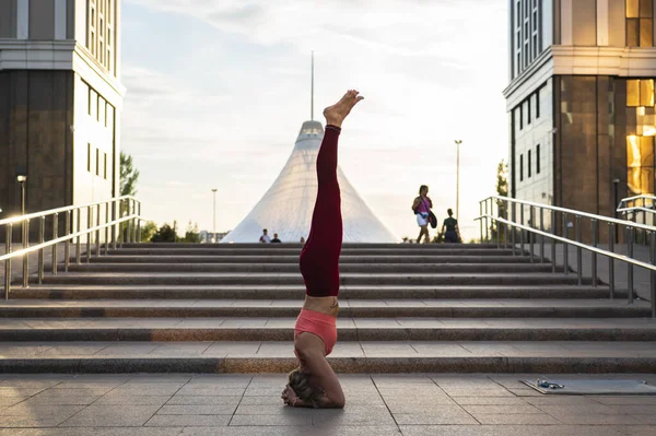 Portrait of a mature woman, 59 years old, doing yoga on a city street. Active sport lifestyle of mature people. Sports in the life of a senior woman. Woman doing a headstand.