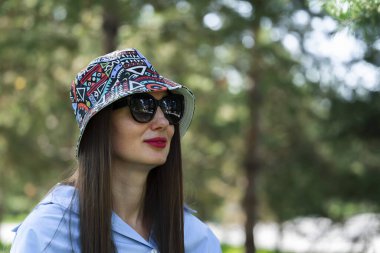 Güneş gözlüklü, uzun sarı saçlı bir kızın yaz portresi. Mavi gömlekli, kot pantolonlu ve panamalı bir kız. Yüksek kalite fotoğraf