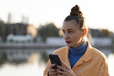 Sonbaharda sokakta elinde akıllı telefon olan genç bir kadın. Yüksek kalite fotoğraf